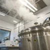 Laboratory autoclave sterilization equipment releasing steam inside a clean scientific lab environment.