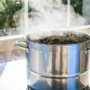 Soil sterilization boiling method using a steaming stainless steel pot filled with soil on a kitchen stove near a bright window.