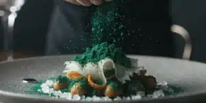 Chef sprinkling cannabis oil powder over a gourmet dish with fine dining presentation.