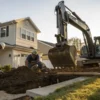 Workers excavating and replacing soil in a residential yard with heavy machinery.