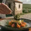 Chef plating a gourmet dish with cannabis leaves and fresh ingredients in a rural setting.