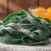 Fresh green spinach tagliatelle pasta dusted with flour and eggs in the background.