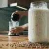 Hemp seed milk in a jar with seeds on the table and a blender in the background.