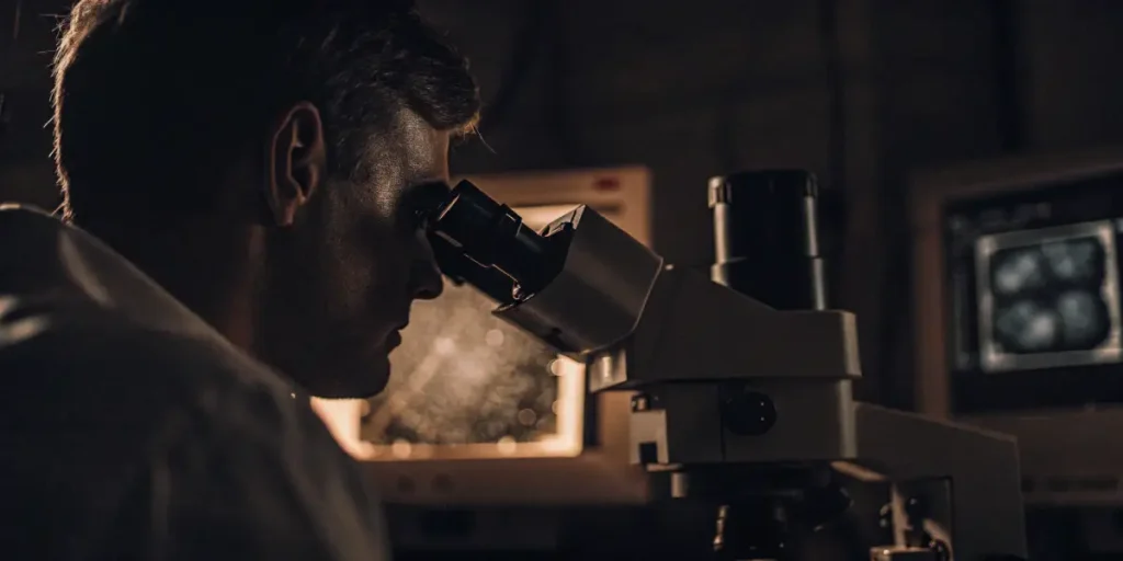 Researcher examining sample under microscope in low-light laboratory setting.