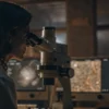 Scientist analyzing samples through microscope with data screens in laboratory.