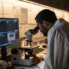 Researcher analyzing samples under microscope with digital screens in laboratory.