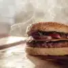 Steaming vegan burger with hemp seeds, lettuce, tomato and cheese on a wooden table.