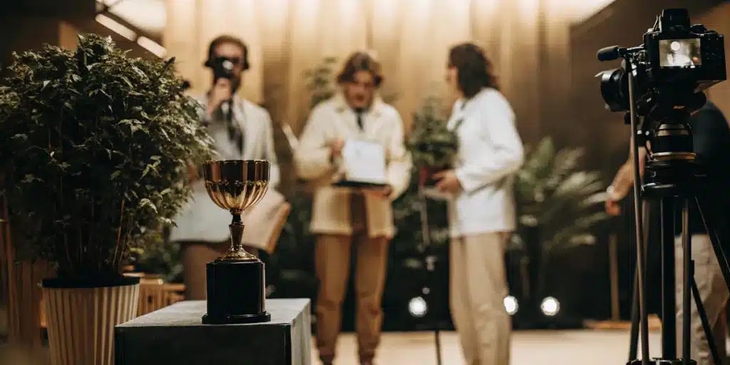 Camera recording a cannabis cup awards ceremony with trophy and finalists on stage.