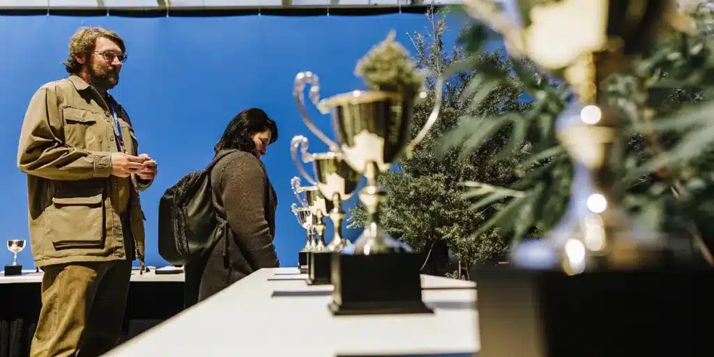 Visitors viewing championship trophies and award-winning cannabis plants at a cannabis cup exhibition.