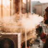 Man exhaling vapor inside an indoor cannabis cultivation facility with ventilation and climate control systems.