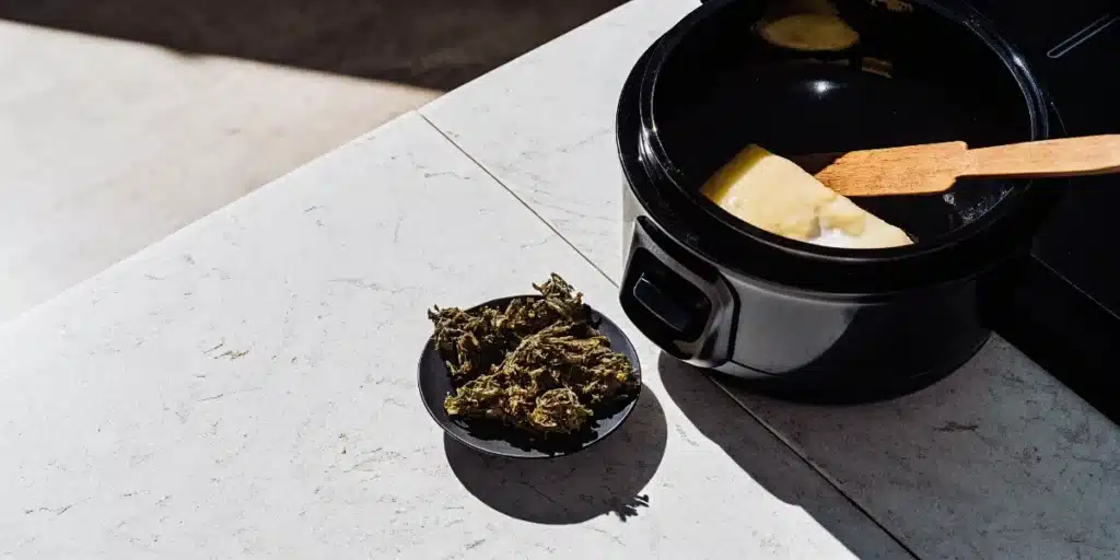 Cannabis flower next to a slow cooker containing melted butter for cannabis infusion.