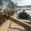 Cannabis pre-roll on canoe with smoke rising over a calm forest lake.