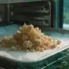 Freshly decarboxylated THCA crumble concentrate on a parchment-lined tray near cannabis plants.