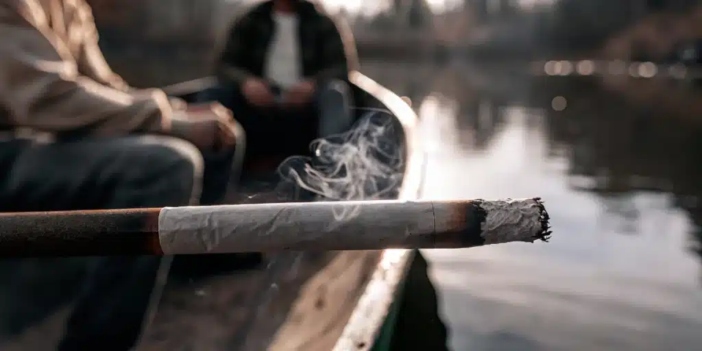 Smoking cannabis joint on lake with visible smoke and people relaxing in a canoe.