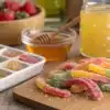 Homemade cannabis gummy candies with infused honey and fresh strawberries on a wooden table.